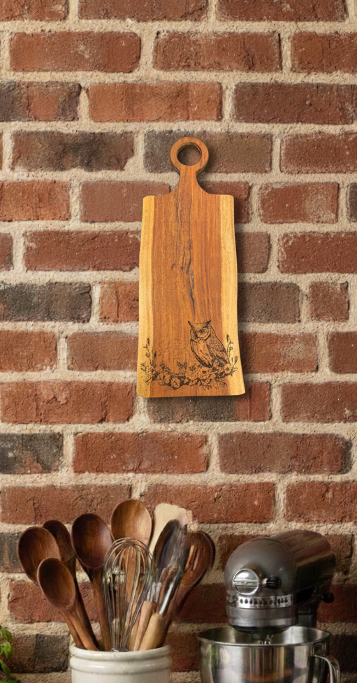 Vertical warm brown wood board featuring an engraved owl, displayed against a textured red brick wall.