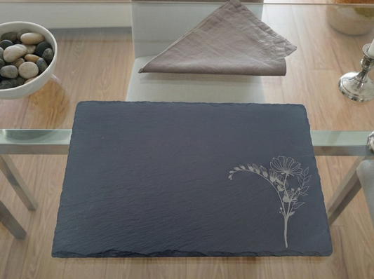 Rectangular charcoal slate placemat with a rough, textured edge and a delicate white floral engraving.