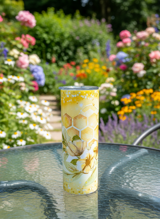 A slim tumbler featuring a honeycomb pattern and flowers on a glass table, set against a vibrant, colourful flower garden.