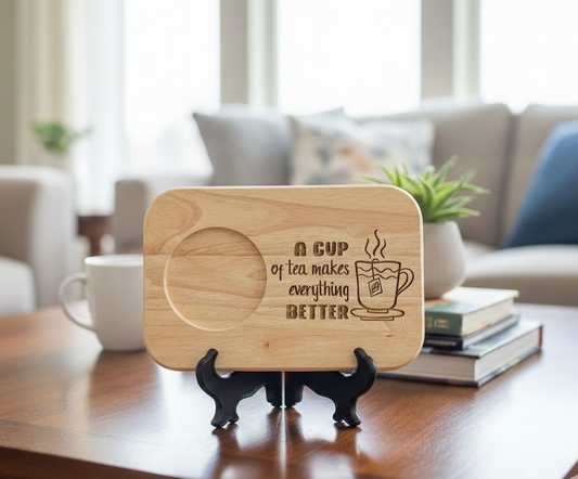 Square light wood display plaque, standing on a black easel. Engraved with a quote; features a circular inset. Blurred living room backdrop.