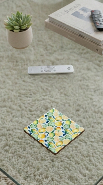 Square coaster with a pale orange and yellow citrus pattern on a glass table above a shaggy cream-coloured rug.