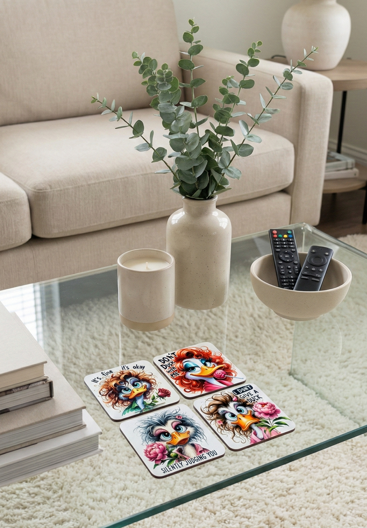 A glass coffee table displaying four novelty duck coasters, a beige vase with fresh eucalyptus, two neutral candles, and a bowl of remotes.