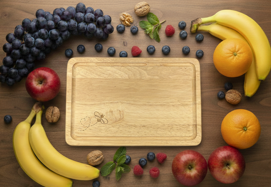 Overhead flat lay: Colourful fruit (grapes, bananas, apples) and walnuts surround a blonde wooden cutting board on dark wood.