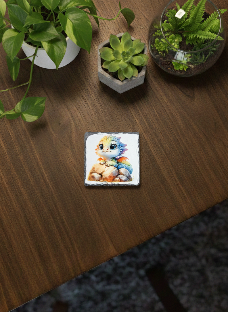 A square, natural slate coaster displaying a pastel, multi-coloured cartoon dragon on a wooden surface.