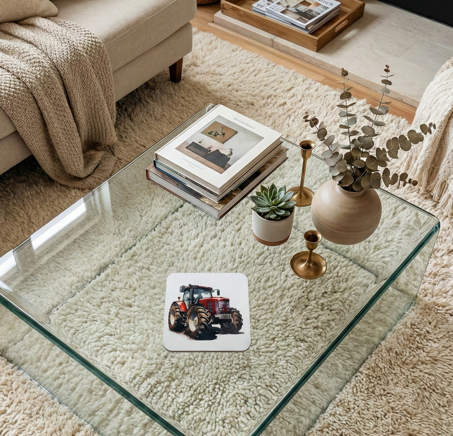 Single white coaster with a red tractor illustration on a glass table, surrounded by books and neutral-coloured decor.