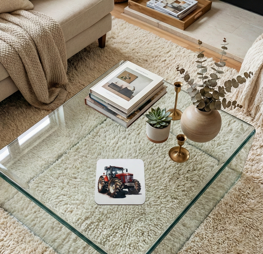 Single white coaster with a red tractor illustration on a glass table, surrounded by books and neutral-coloured decor.