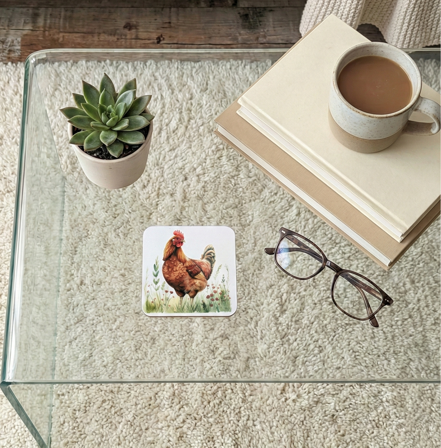 A square coaster illustrating a deep reddish-brown chicken standing amongst green foliage on a clear glass coffee table.