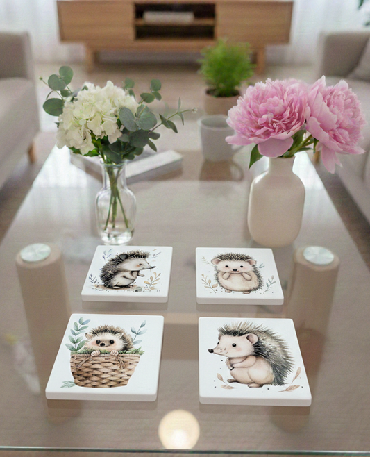 Four white square coasters with hedgehog illustrations on a glass table among pink peonies and white hydrangeas.