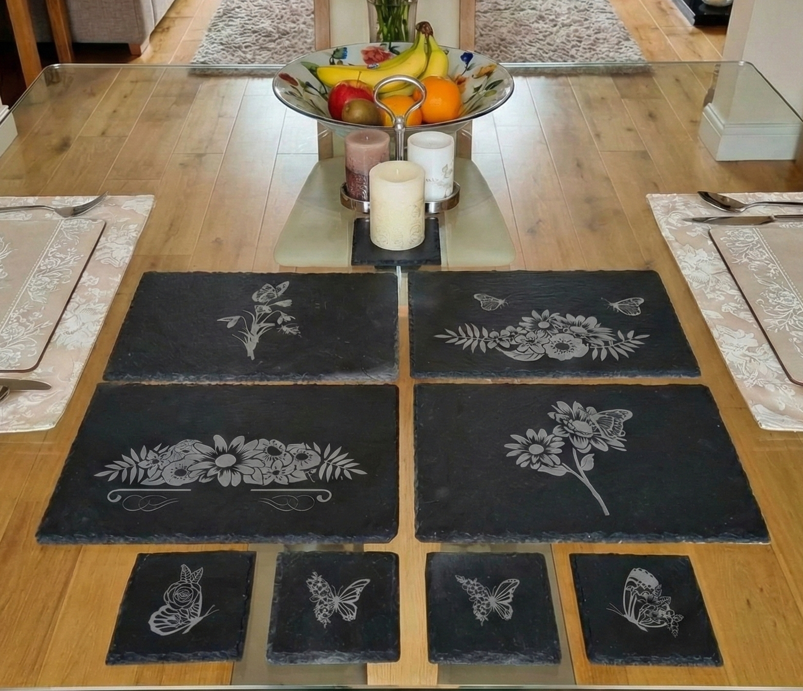 Dark grey rectangular and square slate mats with floral engravings on a glass-topped dining table.