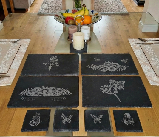 Dark grey rectangular and square slate mats with floral engravings on a glass-topped dining table.