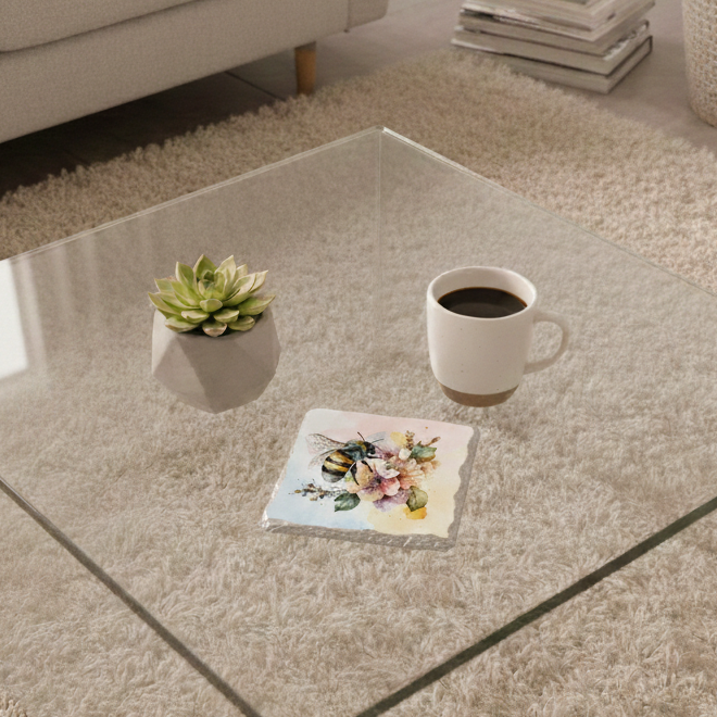 Stone coaster with a large bee over pink watercolour flowers on a glass table with a succulent and white coffee mug.