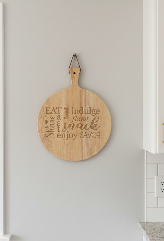 Round light wood serving board, etched with text, hanging by a leather loop on a smooth pale grey wall.