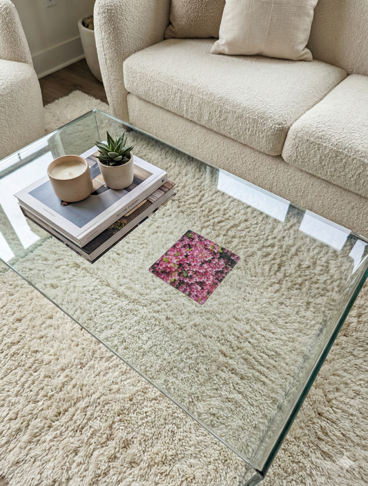 A pink floral coaster on a glass coffee table with books and a succulent, on a plush cream-coloured shaggy rug.