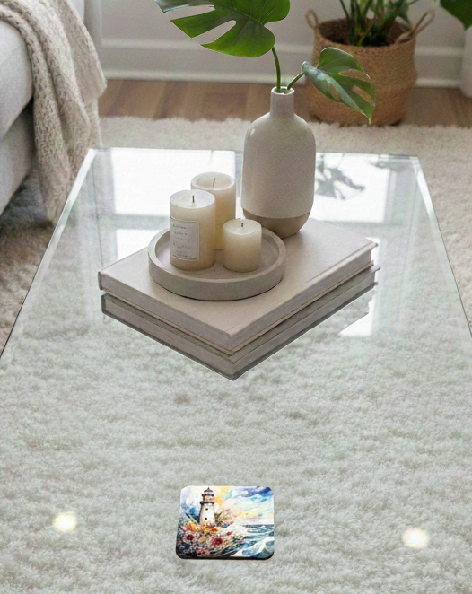 A square coaster with a colourful lighthouse and floral watercolour design is placed on a glass table in a cosy room.