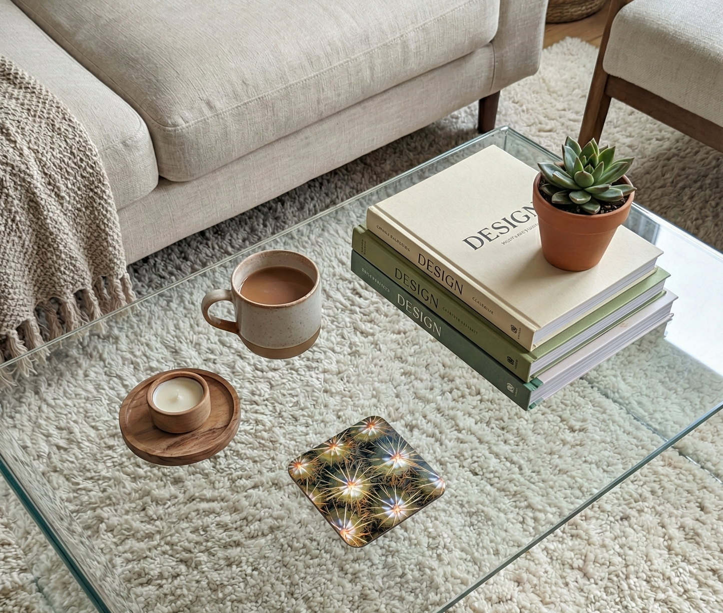A square coaster with a bright, spiky golden-yellow cactus pattern sits beside a speckled cream mug and stacked green books.