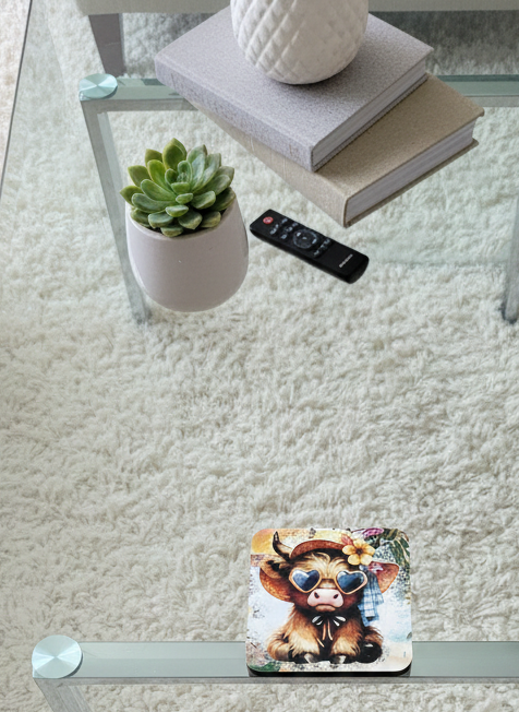 Square coaster showing a baby cow in heart sunglasses on a glass table with a green succulent and white shaggy rug.