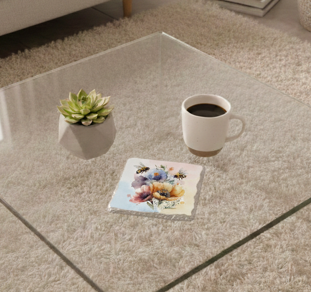 Stone coaster with two bees and colourful watercolour flowers on a glass table beside a succulent and a coffee mug.