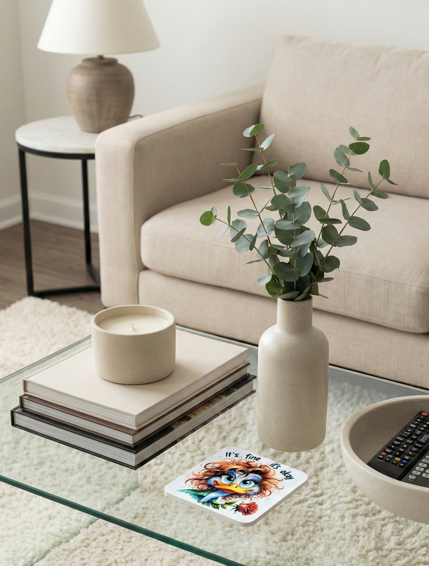 Neutral living room featuring a glass table, speckled beige vase with eucalyptus, a candle, and a cream shag rug.