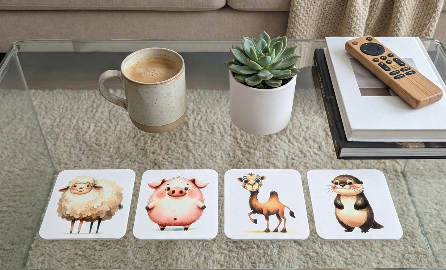 Four square coasters with sheep, pig, camel, and otter designs on a glass table beside a cream mug and succulent.