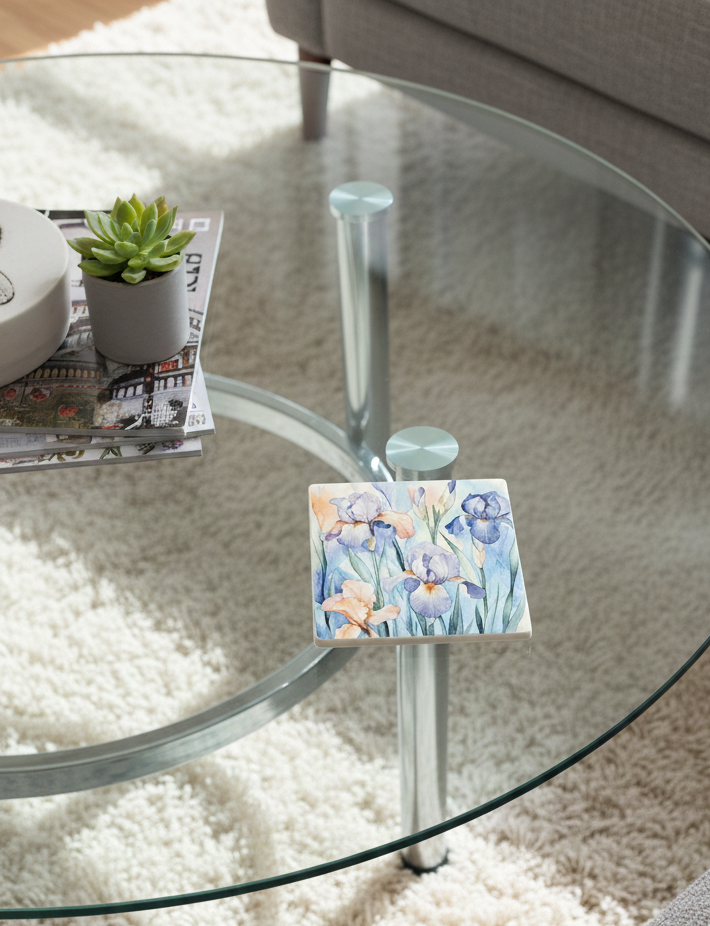 Square coaster with a detailed watercolour painting of blue and peach irises on a glass coffee table in a modern room.
