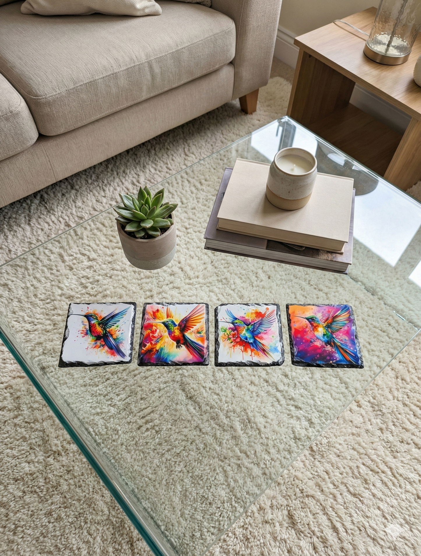 Four square slate coasters featuring vibrant watercolour hummingbirds on a glass table and cream shag-pile rug.