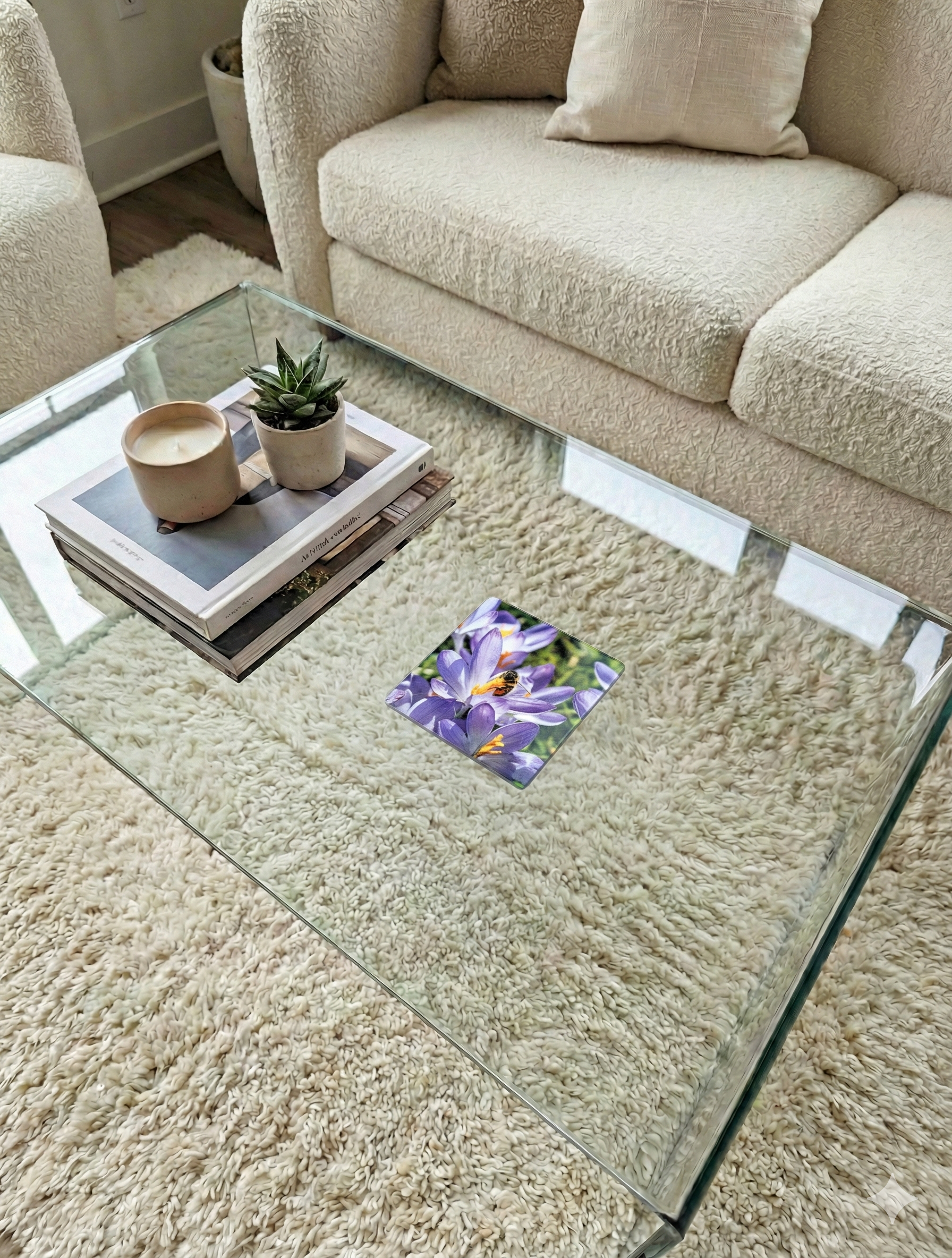 Glass coffee table with a purple crocus and bee coaster, books and a succulent by a cream bouclé sofa.