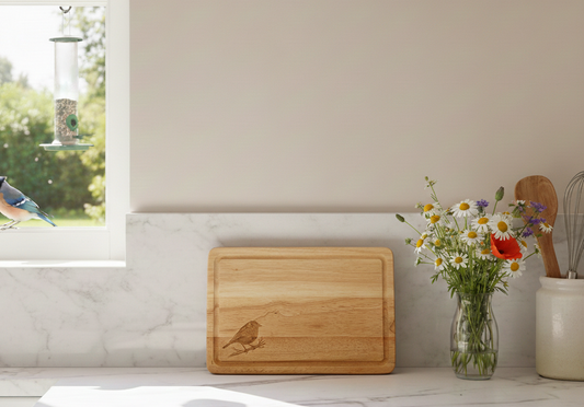 Light brown wooden rectangular chopping board featuring an etched bird motif, resting on a crisp white marble countertop.