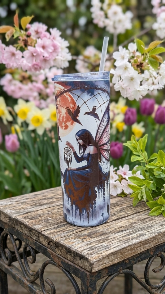Gothic tumbler with a dark fairy and orange moon design on a weathered wooden table, surrounded by pink spring blossom.