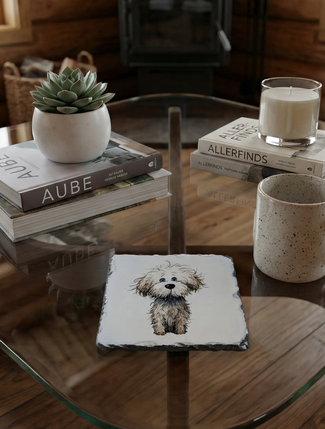 Square slate coaster showing a shaggy grey and white dog, on a glass table with books and a neutral mug.