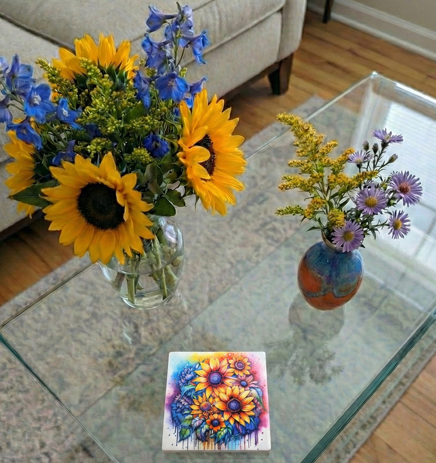 Two vases of flowers and a colourful, vibrant coaster with sunflower designs on a glass coffee table.