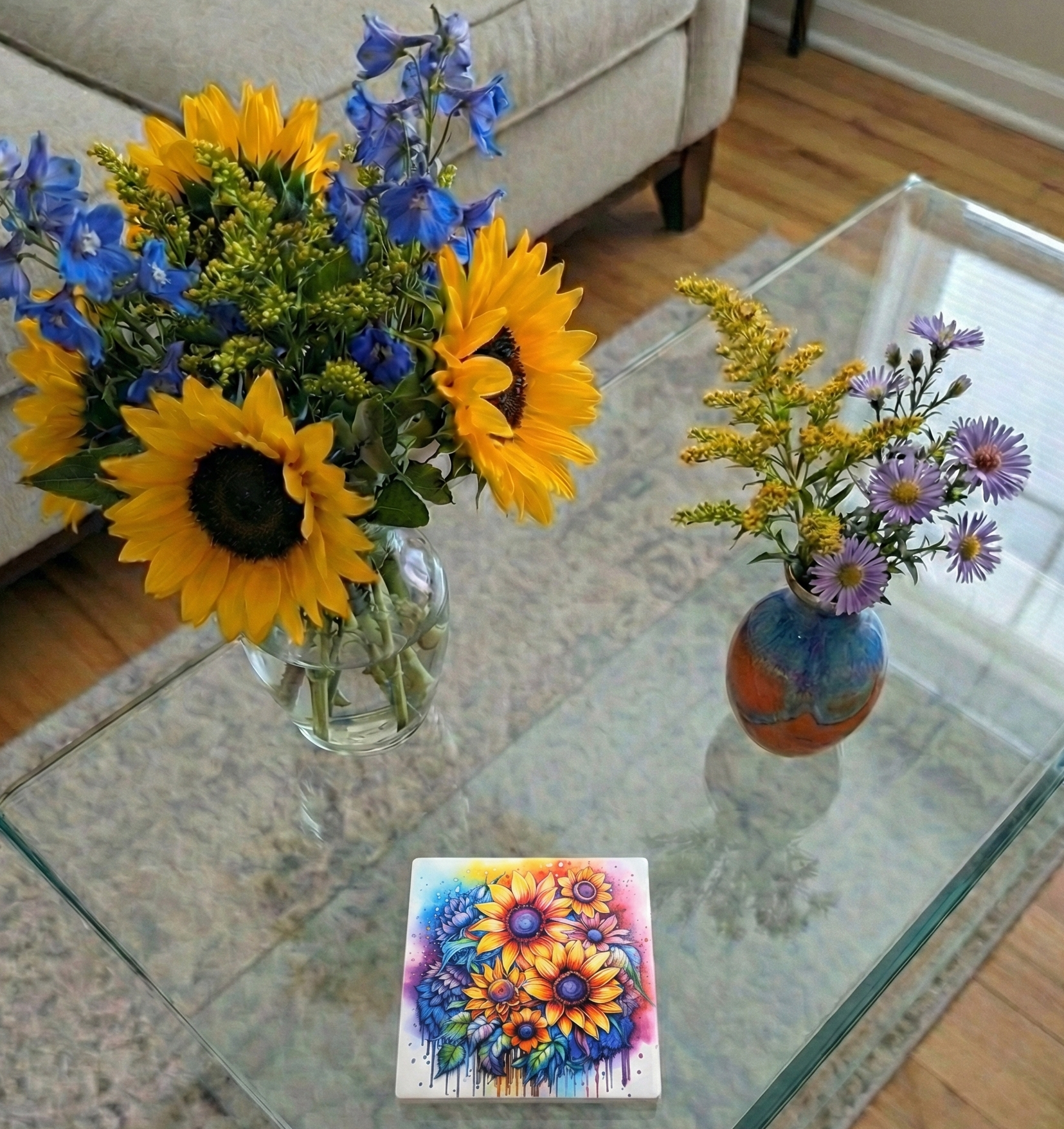 Two vases of flowers and a colourful, vibrant coaster with sunflower designs on a glass coffee table.