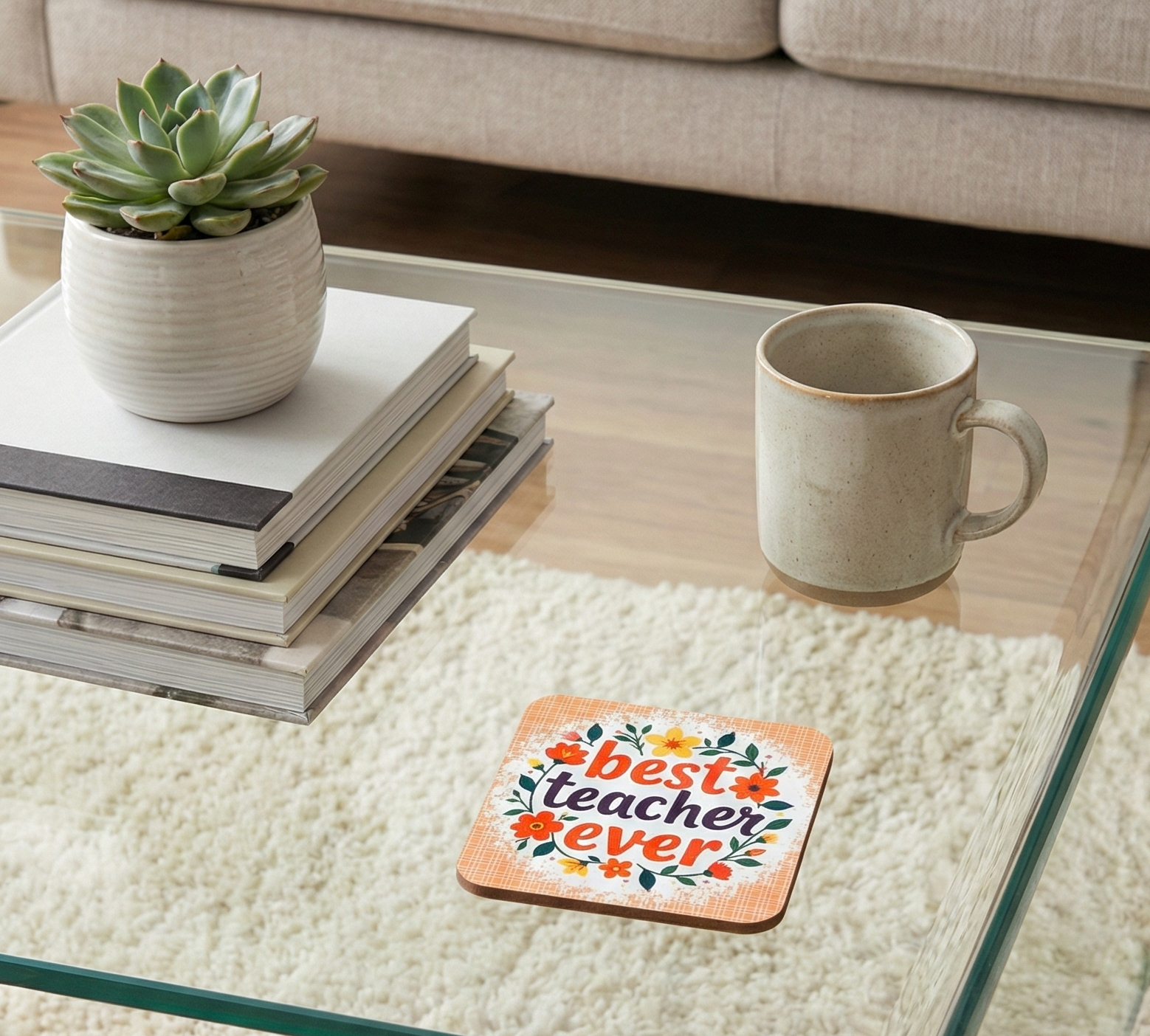Orange checked square coaster with 'best teacher ever' and flowers on a glass table near a green potted succulent.