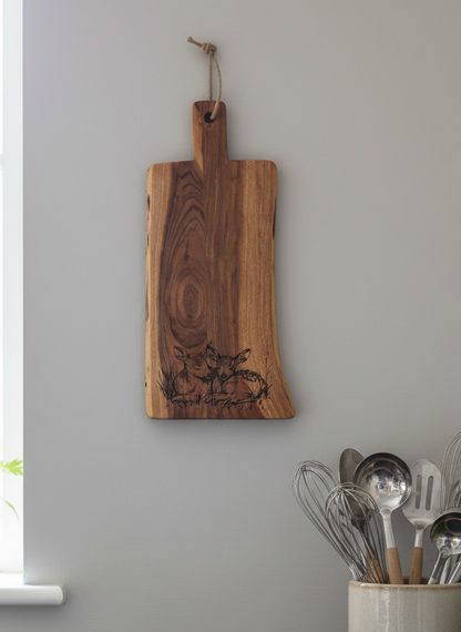 Dark brown, richly grained wooden board with fawn engraving, hung by a rope loop against a smooth pale Grey wall.