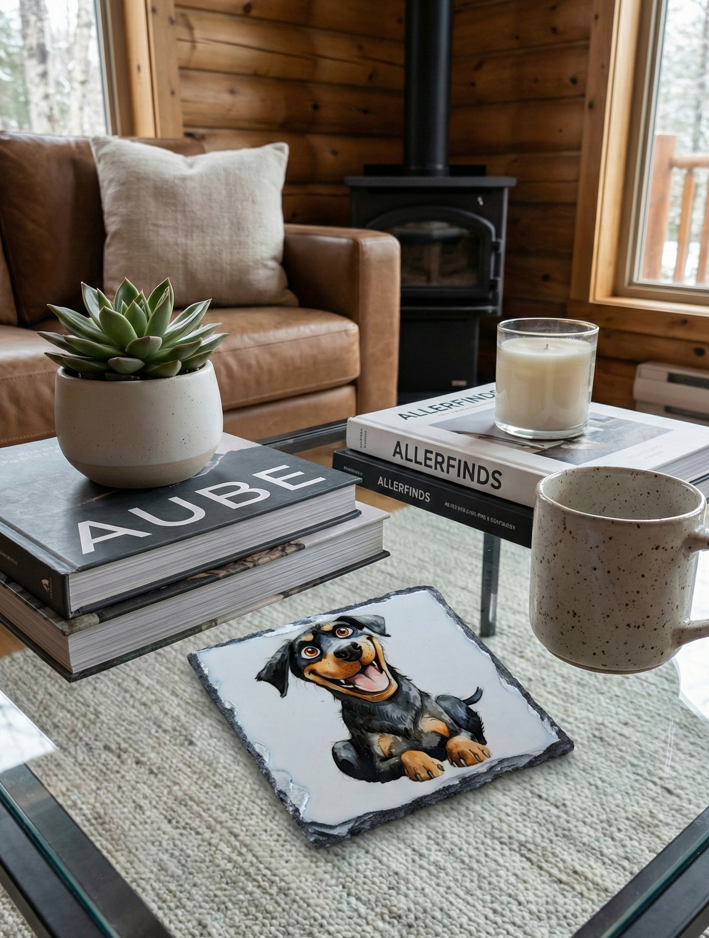 Slate coaster featuring a happy black and tan dog, on a glass table in a cosy room with log walls.