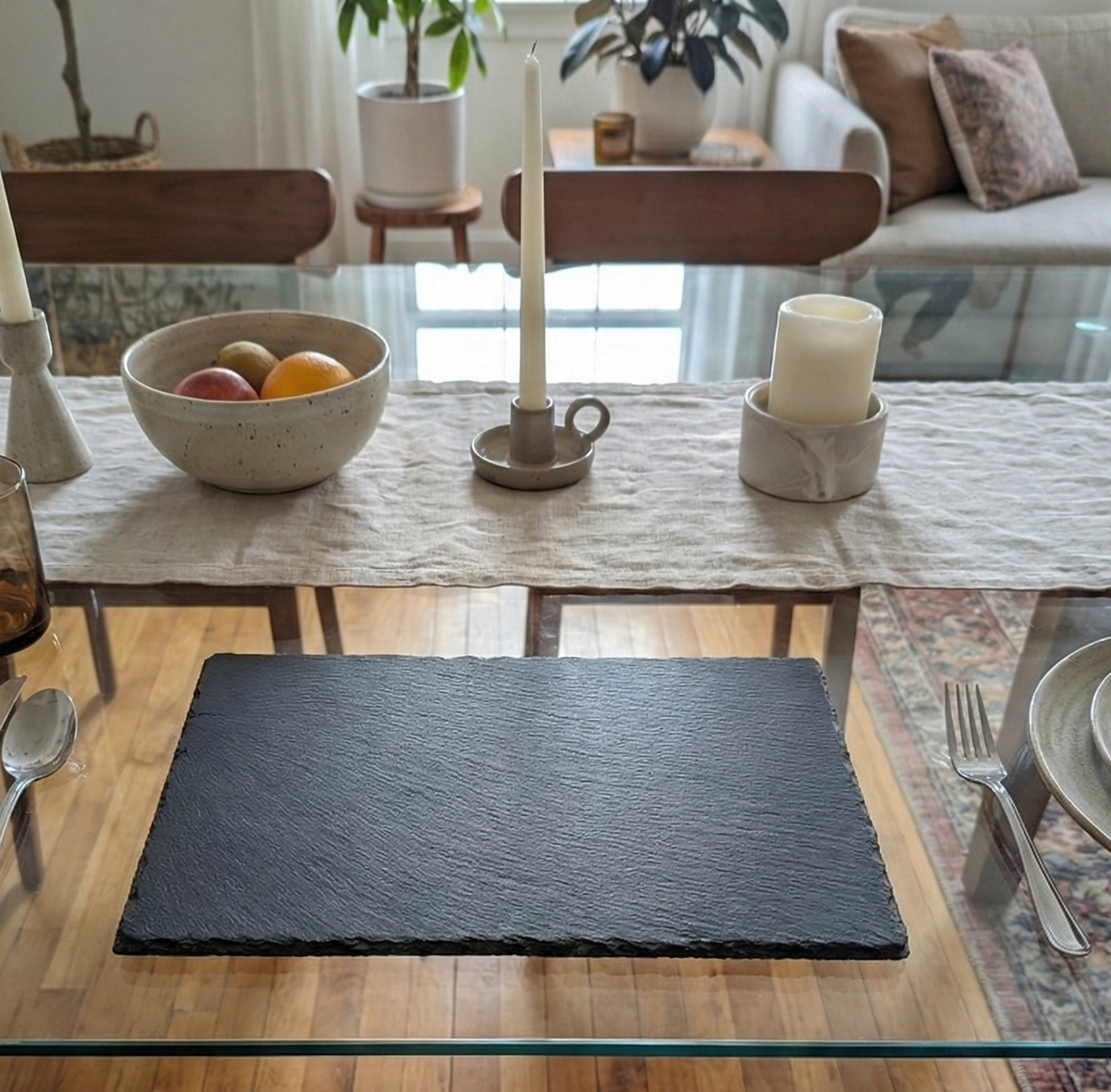 Textured charcoal-grey slate placemat on a glass table with silver cutlery and neutral-coloured decor.