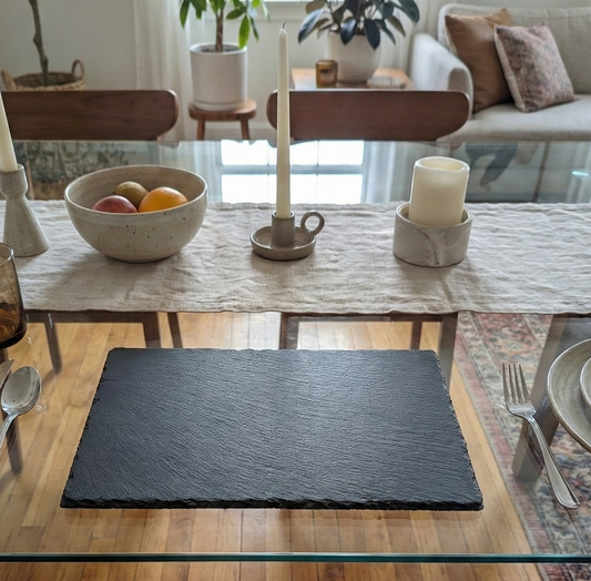 Textured charcoal-grey slate placemat on a glass table with silver cutlery and neutral-coloured decor.