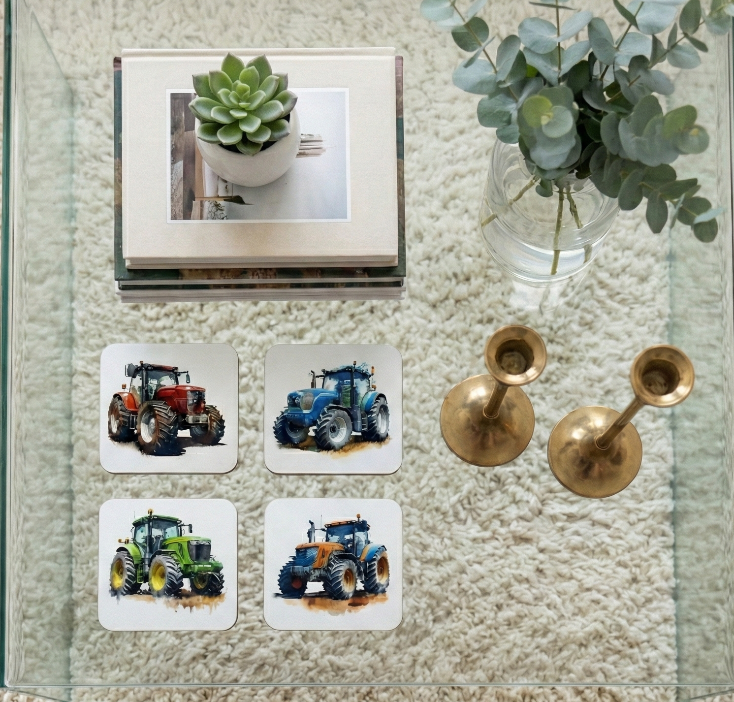 Top-down view of four white coasters with colourful tractor illustrations on a glass table over a cream shaggy rug.