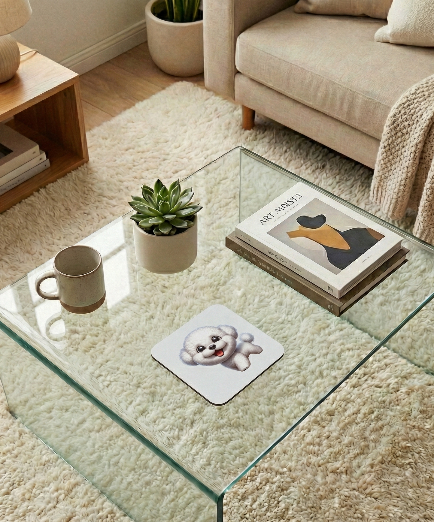 Fluffy white Bichon Frise dog coaster on a glass table. A speckled mug and art books are in the background.