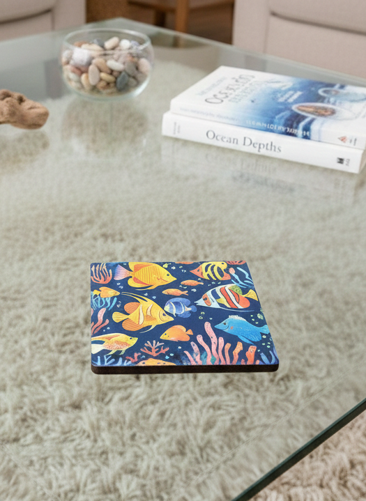 Square coaster with vibrant yellow and orange fish on a dark blue background, resting on a glass coffee table.