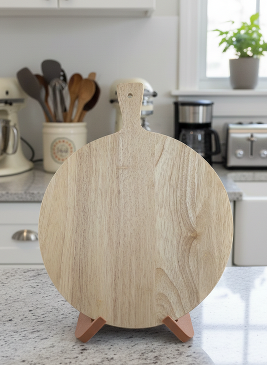 A round, pale wood cutting board with visible grain, sitting upright on a small copper-tone stand atop a speckled grey counter.