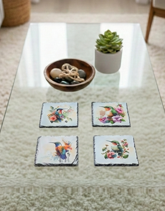 Four square slate coasters displaying colourful watercolour hummingbird designs, set upon a glass table and cream shag rug.