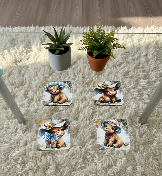 Four square coasters with colourful baby cow designs on a glass table over a fluffy white rug and green plants.