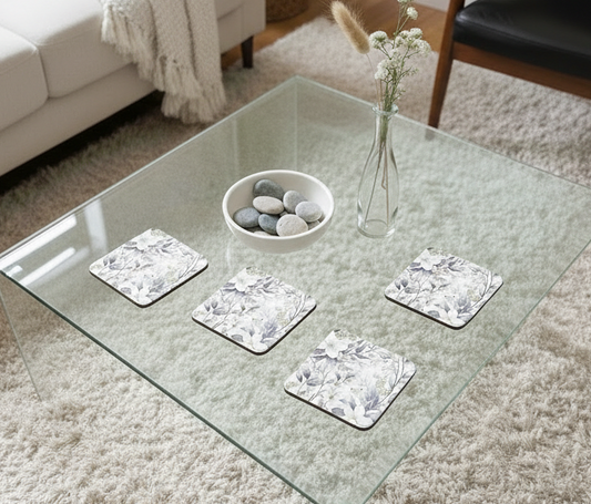Four square coasters with grey floral patterns on a glass table, with a textured cream rug shown underneath.