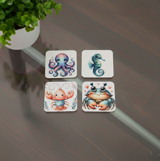 Four square coasters with colourful sea creature illustrations on a dark table, next to a small green plant.