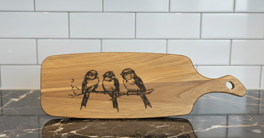 Smooth, light brown wooden serving board with rounded edges, featuring an engraved sketch of three perched birds.